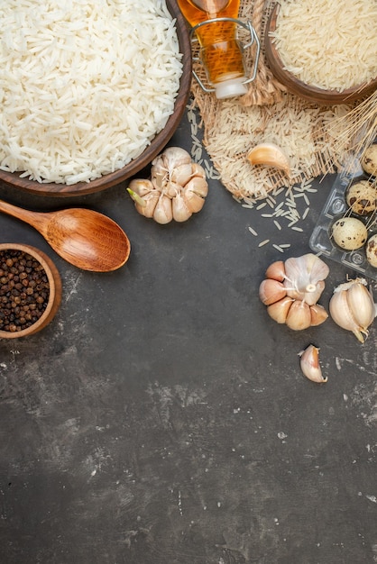 Vista vertical de tigelas marrons de arroz longo perfeitas em toalha de cor nude, garrafa de óleo caída, pimentas de alho no topo em fundo escuro