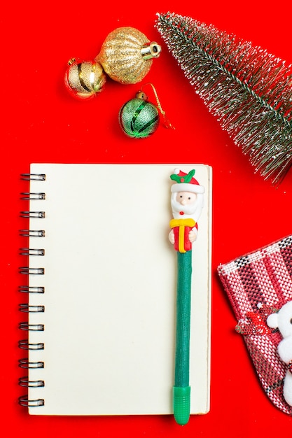 Foto grátis vista vertical do caderno espiral com caneta e acessórios de decoração para árvore de natal em fundo vermelho