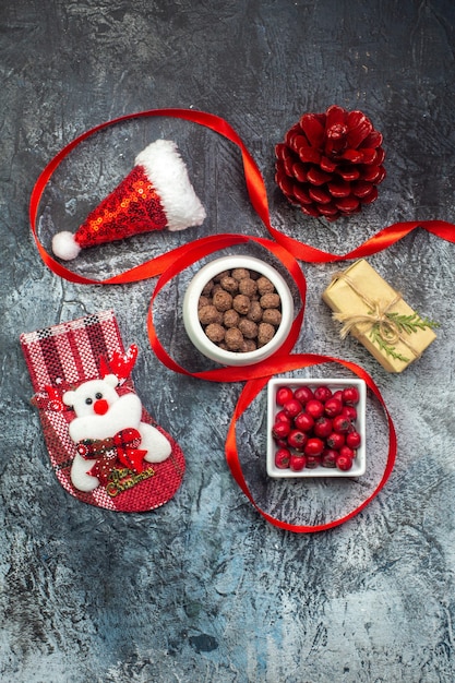 Vista vertical do chapéu de Papai Noel e presente de cone de conífera vermelha com meia de chocolate de ano novo na superfície escura