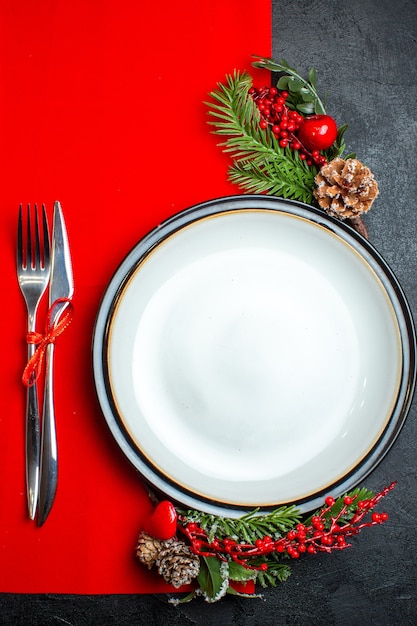 Vista vertical do fundo de Natal com acessórios de decoração de prato, ramos de abeto e talheres em um guardanapo vermelho