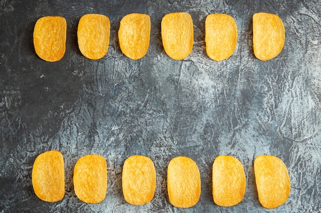 Visualização horizontal de cinco chips assados crocantes alinhados em uma mesa cinza.