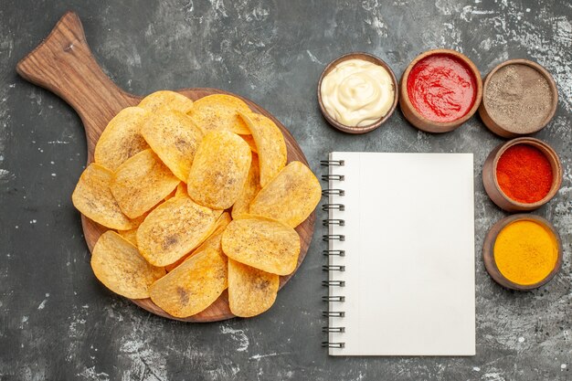 Visualização horizontal de temperos de batata frita e maionese com ketchup e caderno na mesa cinza