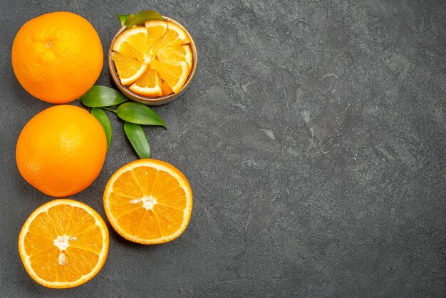 Visualização horizontal de um conjunto de laranjas amarelas inteiras e picadas na mesa escura