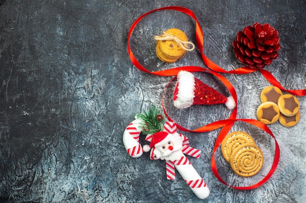 Visualização horizontal do chapéu de papai noel e biscoitos para presente de cone de conífera vermelha chocolate na superfície escura