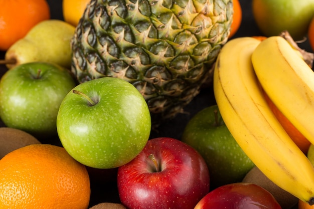Vitaminas coloridas de frutas frescas ricas maduras maduras maçãs verdes bananas e outros na mesa cinza