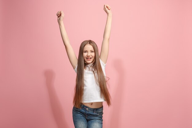 Vitória adolescente feliz de sucesso comemorando ser um vencedor. Imagem dinâmica do modelo feminino caucasiano na parede rosa do estúdio. Vitória, conceito de prazer. Conceito de emoções faciais humanas. Cores da moda