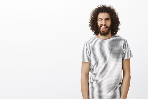 Viva a vida ao máximo. Retrato de homem bonito despreocupado com barba e cabelo encaracolado, mostrando a língua e piscando o olho