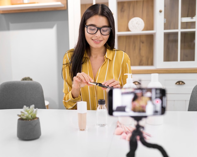 Vlogger feminina em casa com smartphone e rímel