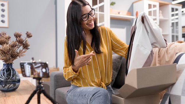 Vlogger feminina em casa desembalando roupas com smartphone