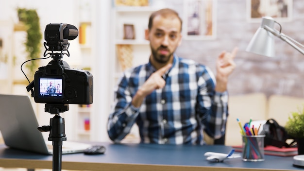 Vlogger sentado à mesa na sala de estar conversando e olhando para a câmera. Gravação de influenciador famoso para mídia social.