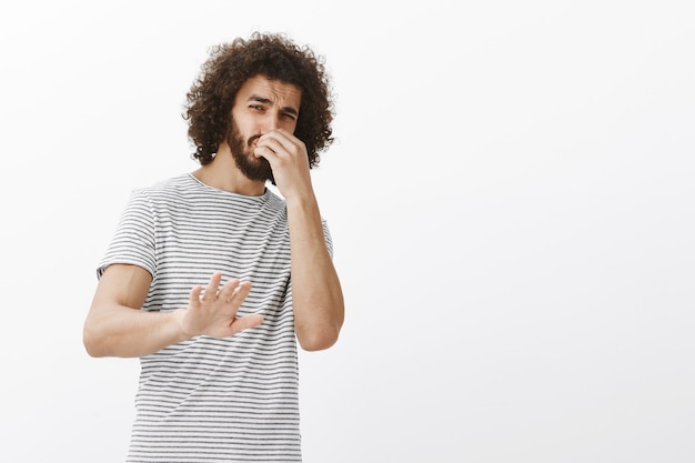 Foto grátis você fede, não se aproxime. retrato de um cara bonito com nojo e não gosta de penteado afro, inclinando-se para trás e puxando a palma da mão para parar ou sem gesto