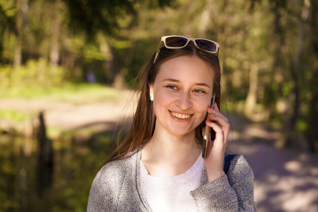 Você, uma linda jovem com óculos de sol anda e fala ao telefone em um dia ensolarado de primavera