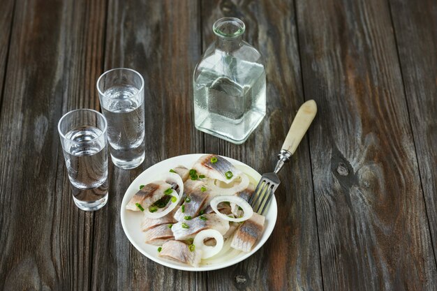 Vodka com arenque salgado e cebola na superfície de madeira. Álcool bebida artesanal pura e petisco tradicional. Espaço negativo. Comemorando comida e deliciosa.