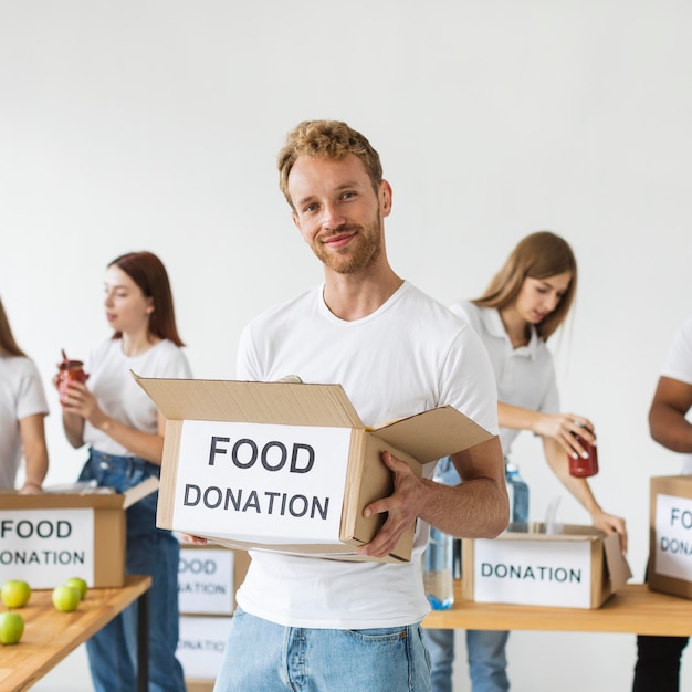 Voluntário sorridente segurando uma caixa de doações de alimentos