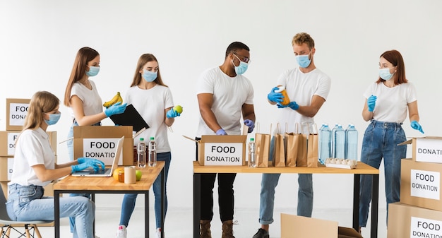 Voluntários com máscaras médicas e luvas preparando caixas com alimentos para doação