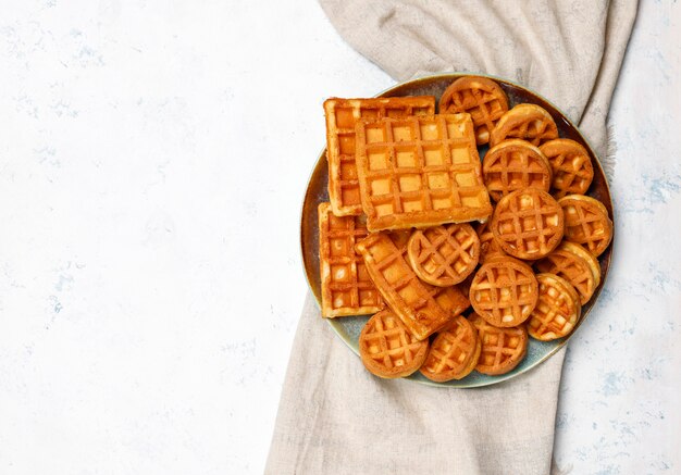 Waffles belgas tradicionais com bagas frescas e mel na superfície de concreto cinza.