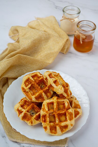 Waffles belgas tradicionais, laranjas pigmentadas e mirtilos, molho e xícara de café no café da manhã doce, composição sobre fundo claro.