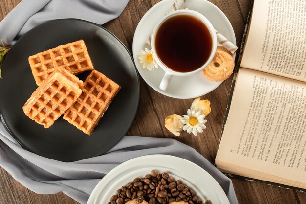 Waffles em um pires preto e uma xícara de chá. vista do topo