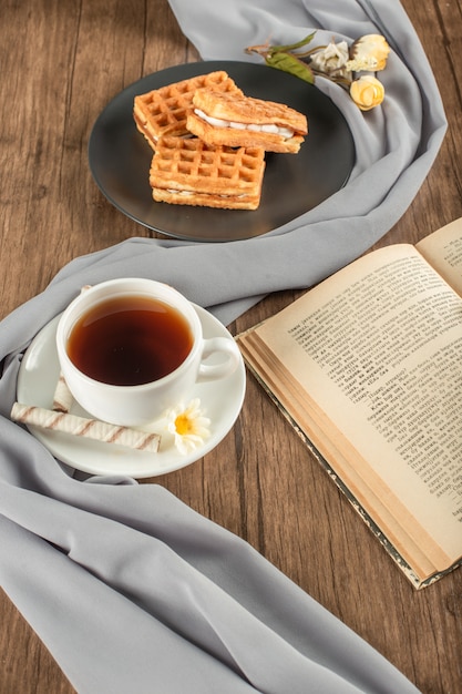 Waffles em um pires preto, uma xícara de chá e um livro.