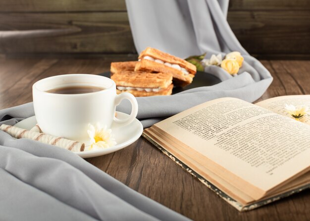 Waffles em um pires preto, uma xícara de chá na mesa de madeira.