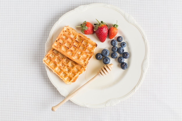 Waffles; morango e mirtilos na placa de cerâmica sobre a toalha de mesa