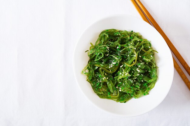 Wakame Chuka ou salada de algas com sementes de gergelim em tigela na mesa branca. Comida japonesa tradicional. Vista do topo. Configuração plana