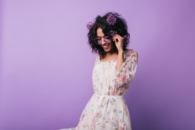 Foto grátis winsome garota africana posando em um vestido com padrão floral. retrato de uma senhora negra despreocupada com alliums no cabelo.