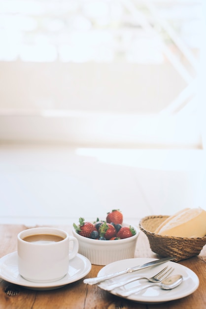Foto grátis xícara de café com frutas frescas e talheres na placa contra o fundo de madeira