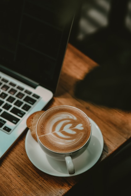 Xícara de café com leite ao lado de um laptop