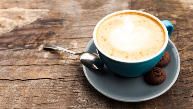 Xícara de café com leite com deliciosos biscoitos na mesa de madeira