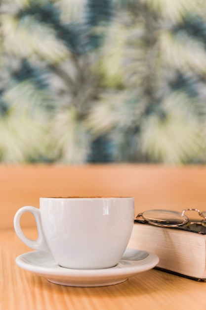 Foto grátis xícara de café com óculos e livro na mesa de madeira