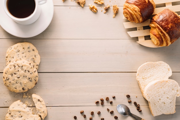 Xícara de café com pães e biscoitos na mesa de madeira