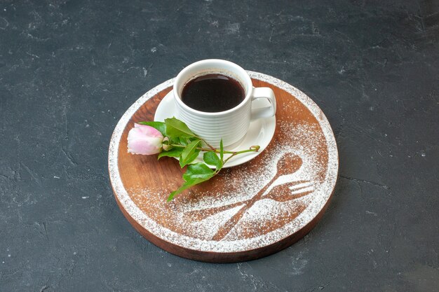 Xícara de café de frente com flores e farinha em uma parede escura