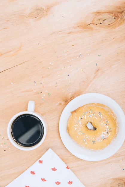 Xícara de café; donut com sprinkles e lenço de papel no pano de fundo texturizado de madeira
