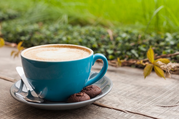 Xícara de café e biscoitos na superfície de madeira com fundo de natureza verde de desfocagem