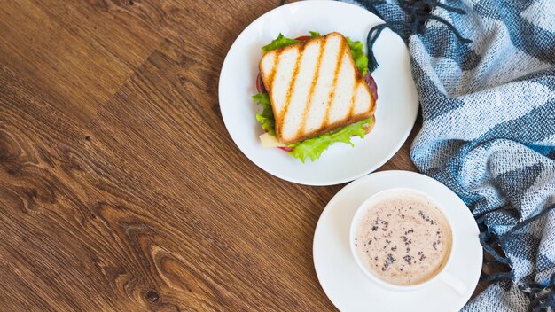 Xícara de café e sanduíche grelhado com guardanapo na mesa de madeira