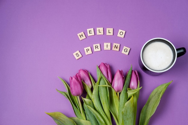 Xícara de café e tulipas roxas sobre fundo violeta e letras de madeira conceito de primavera vista superior do espaço de cópia plana