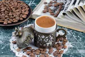 Foto grátis xícara de café espumoso, prato de grãos de café e livro sobre a mesa de mármore.