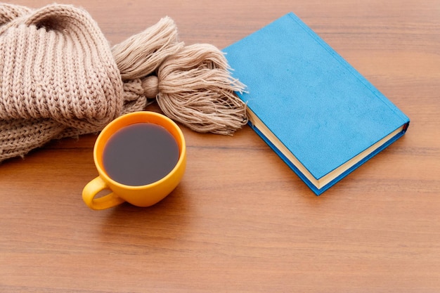 Xícara de café, lenço de malha e livro sobre fundo de madeira