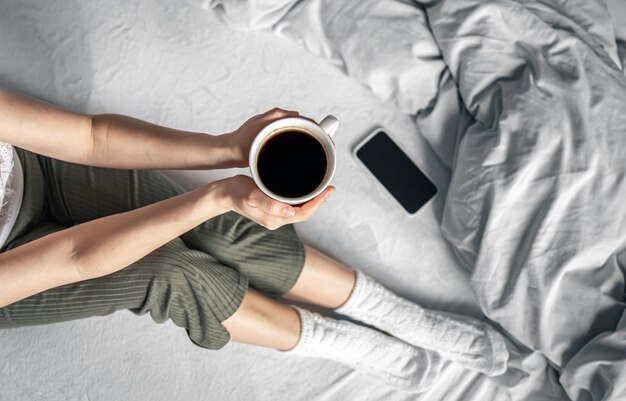 Xícara de café na cama na vista superior das mãos femininas
