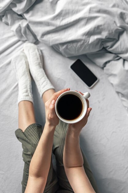 Xícara de café na cama na vista superior das mãos femininas