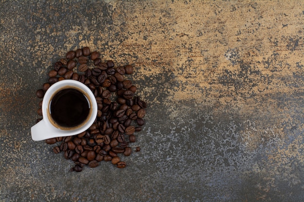 Xícara de café preto com grãos de café na superfície de mármore.