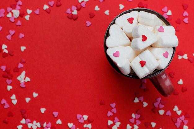 xícara de café quente com marshmallows em forma de coração e confetes no vermelho