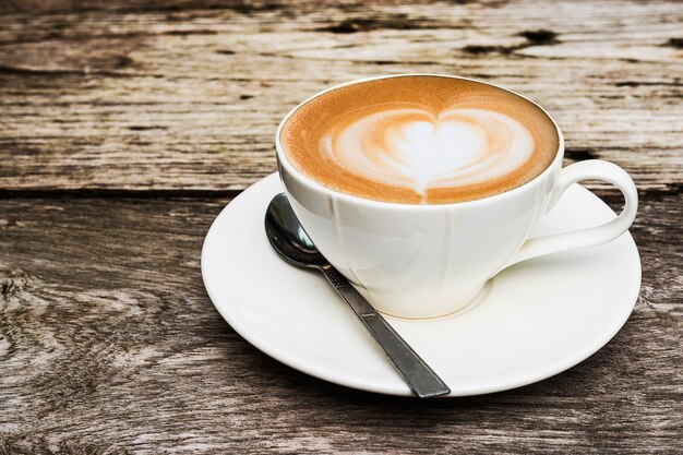 Xícara de café quente vintage com decoração de arte latte agradável na mesa de textura de madeira velha