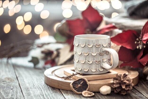 Xícara de café sobre bokeh de luzes de Natal em casa na mesa de madeira com flores na parede e decorações. Decoração de férias, Natal mágico