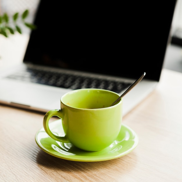 Xícara de café verde e laptop aberto na mesa de madeira