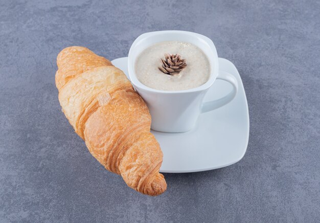 Xícara de Cappuccino e croissant no café da manhã em fundo cinza.