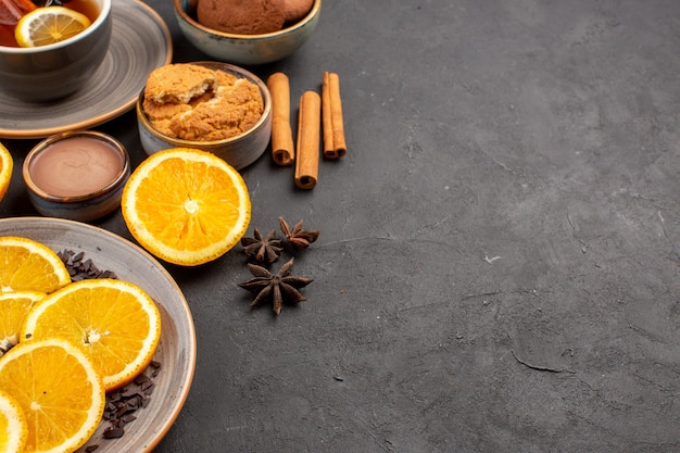 xícara de chá com biscoitos e laranjas frescas fatiadas no escuro