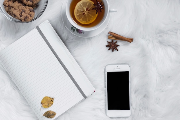 Foto grátis xícara de chá com biscoitos perto de bloco de notas e smartphone