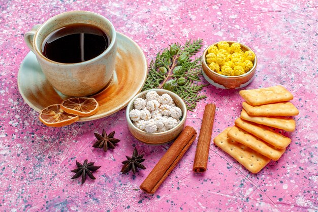 Xícara de chá com doces de canela e biscoitos na mesa rosa